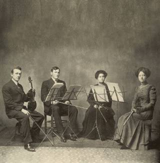 Four student musicians from 1911 pose for a photo with instruments