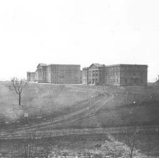 Three brick buildings, each several stories high, stand isolated on a treeless prairie