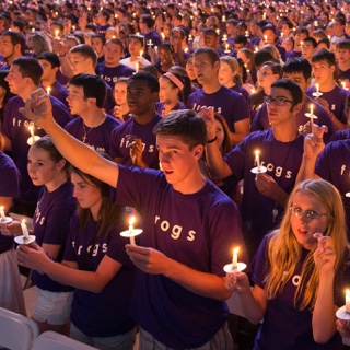 A large group of students — all with purple Go Frogs shirts and each with a lit candle — gather during the Chancellor's Assembly