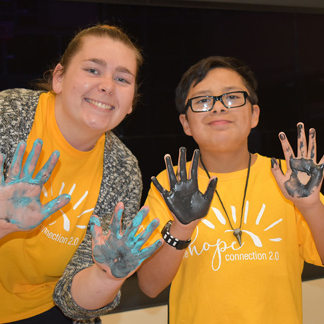 A teacher and young student show evidence of their painting activity, palms coated in finger paint