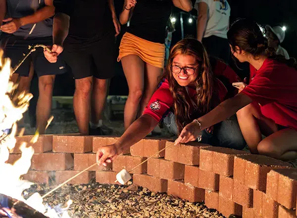 Students roast marshmallows on a giant fire pit